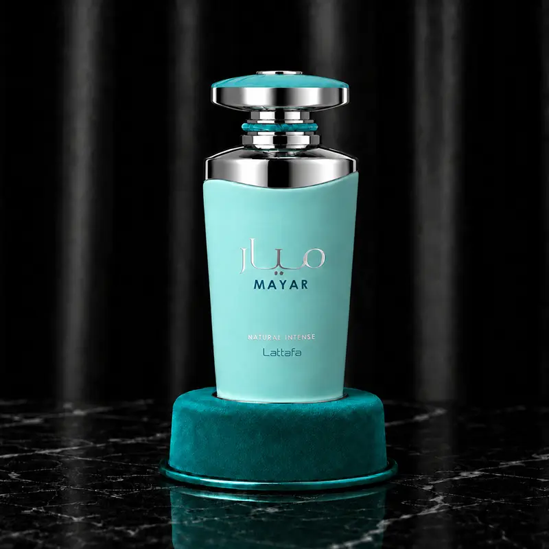 Turquoise perfume bottle standing on a round teal velvet pedestal against black drapery